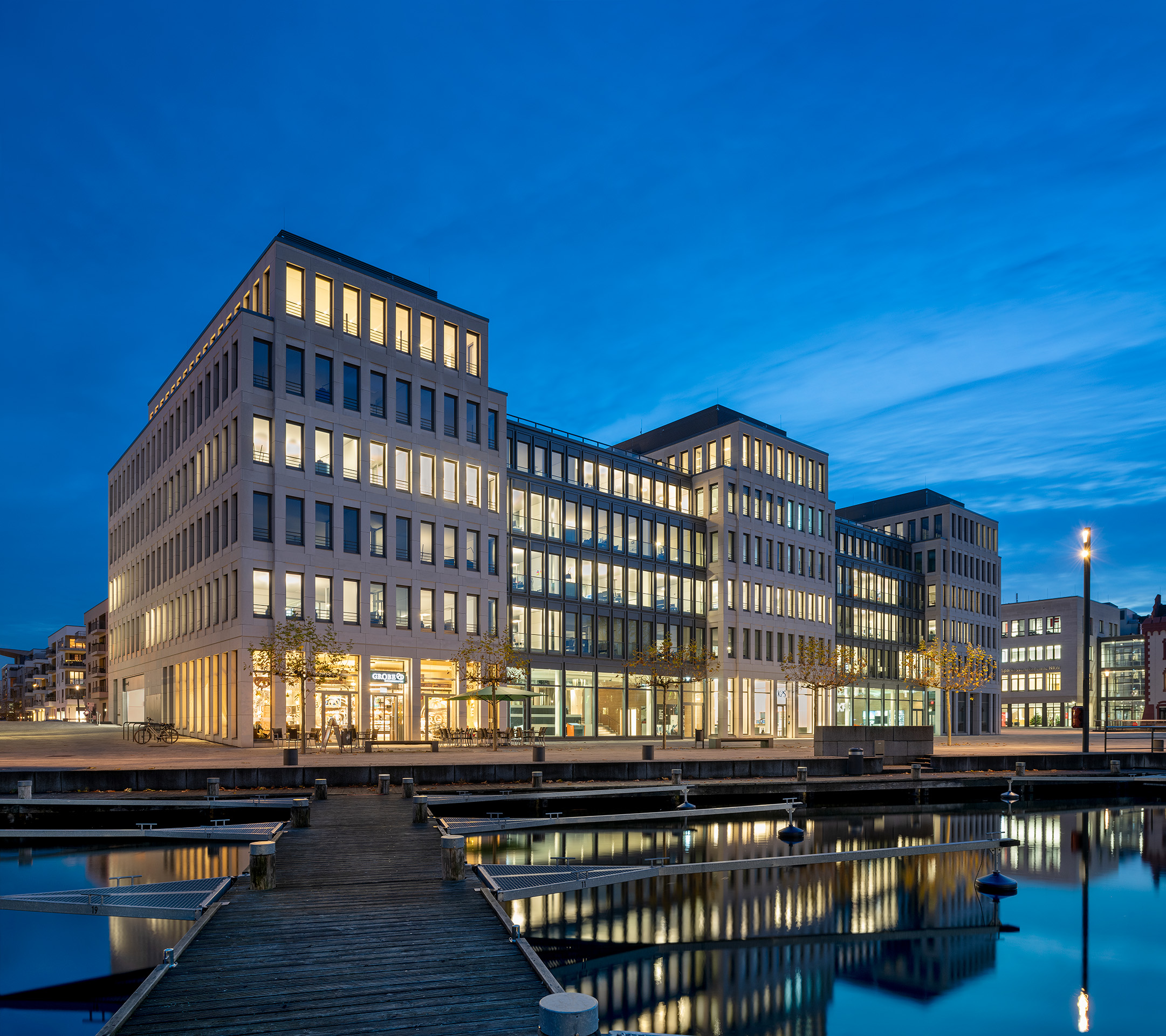 Bürogebäude des Projekts KPS am Dortmunder Hafen bei Abenddämmerung mit beleuchteter Fassade und Wasserbecken