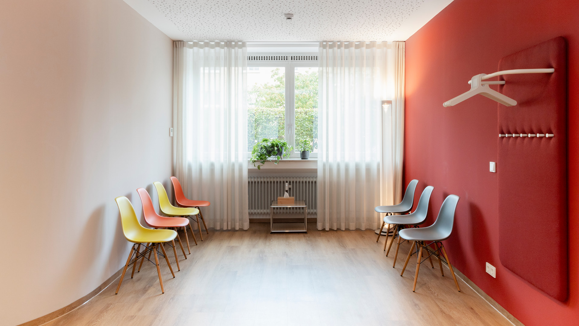 Wartebereich mit farbigen Stühlen, geschwungener Wand und integrierter Garderobe.