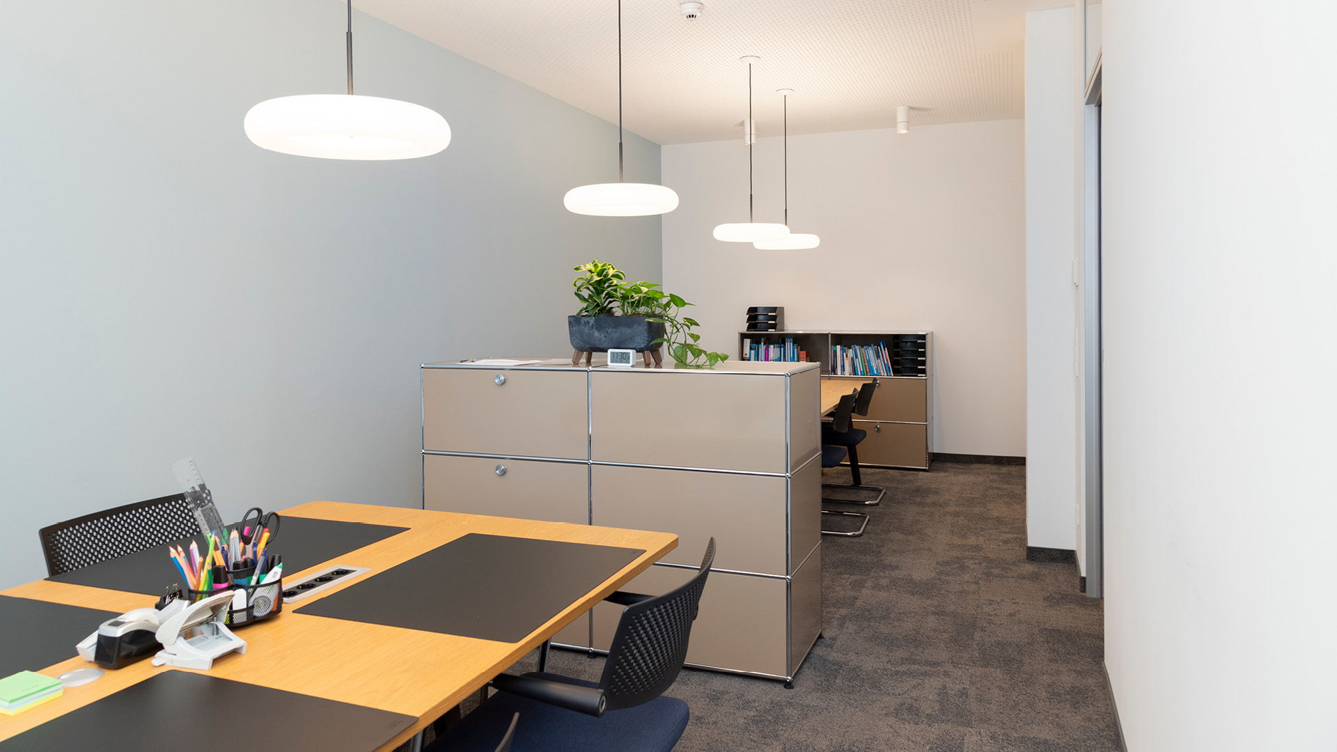 Arbeitsbereich mit großem Arbeitstisch, USM Haller Stauraummöbeln und Pendelleuchten.