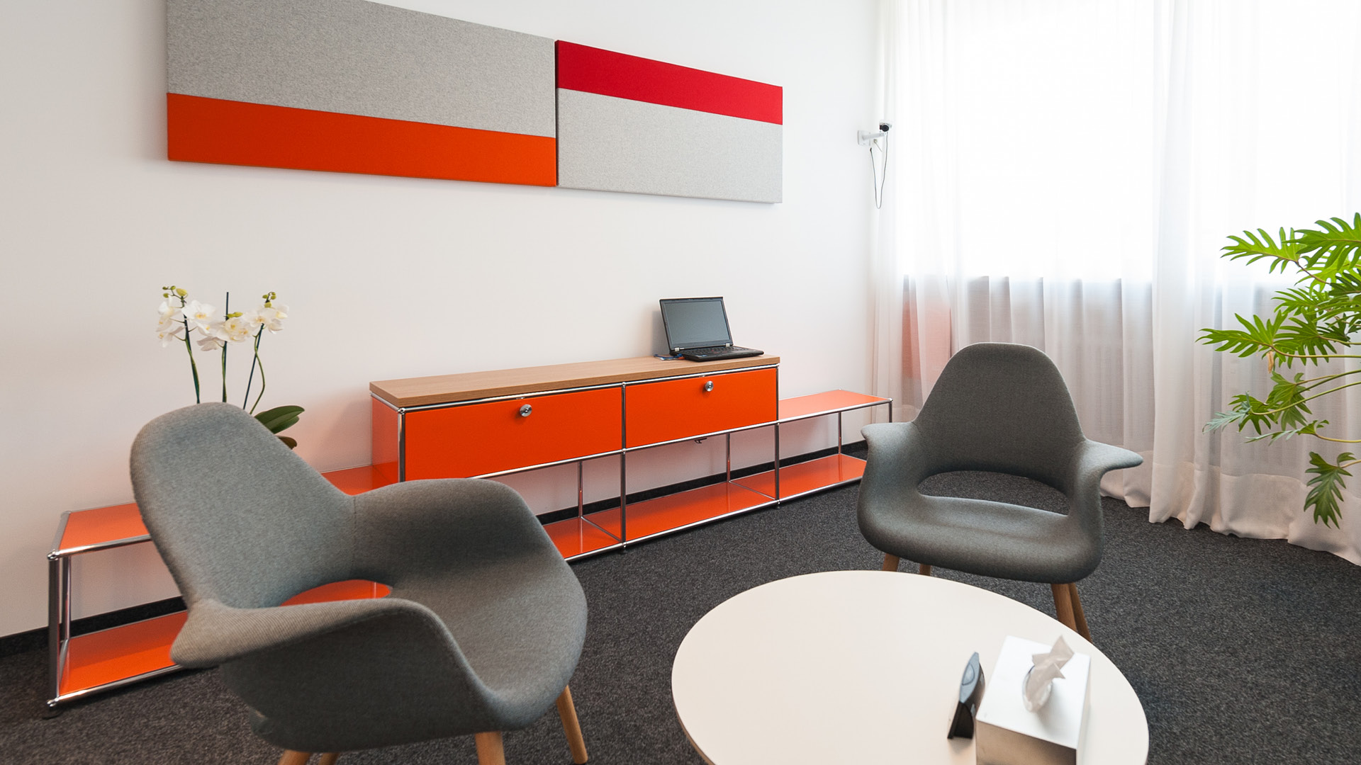 Therapieraum im CIP Erlangen mit grauen Sesseln, orangefarbenem USM Haller Sideboard und Akustikelementen.