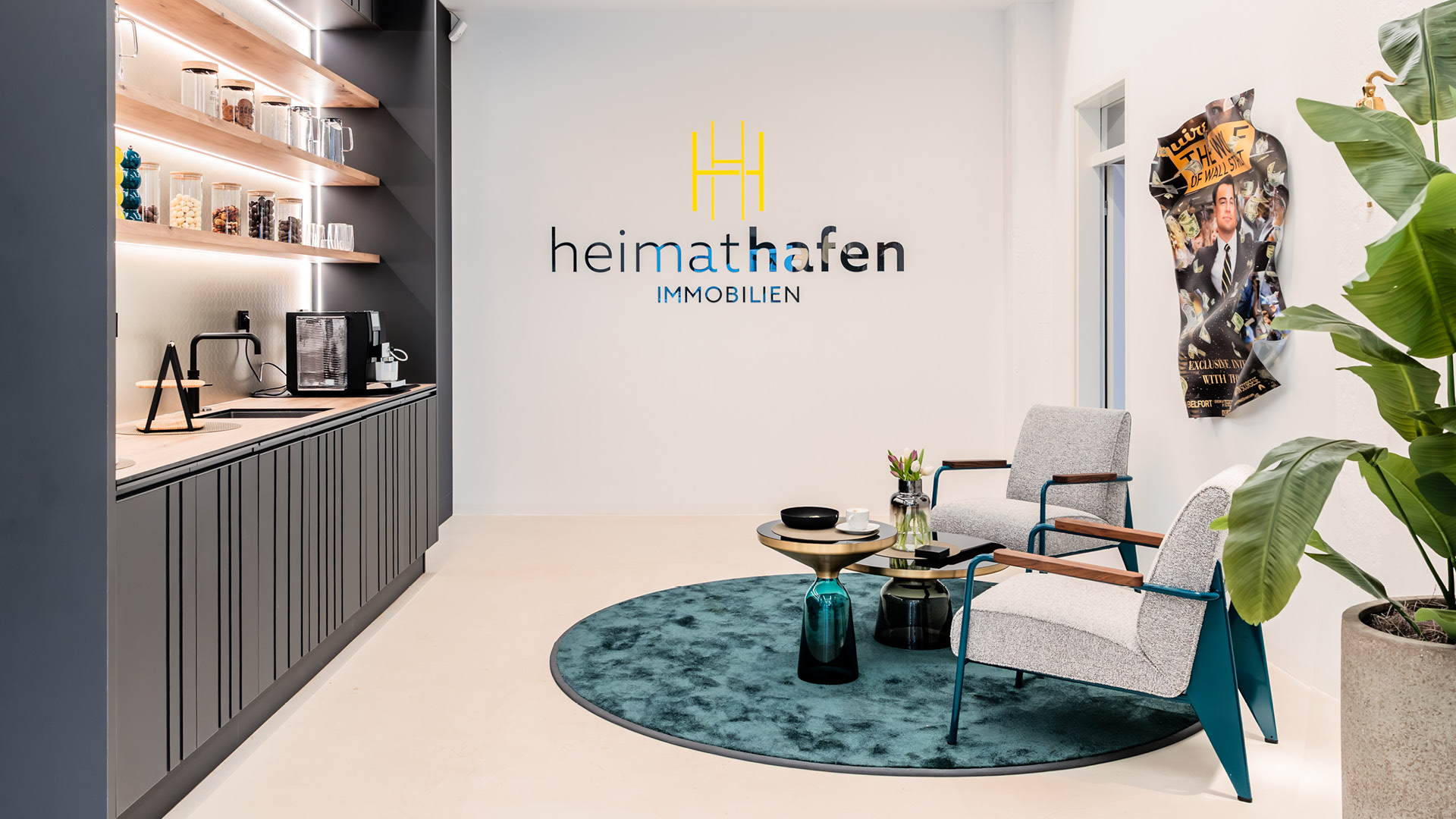 Modern gestalteter Büro- und Loungebereich im Referenzprojekt Heimathafen Immobilien in Münster mit integrierter Teeküche, Sitzgruppe und hochwertiger Innenarchitektur für zeitgemäßes Arbeiten und Empfang.