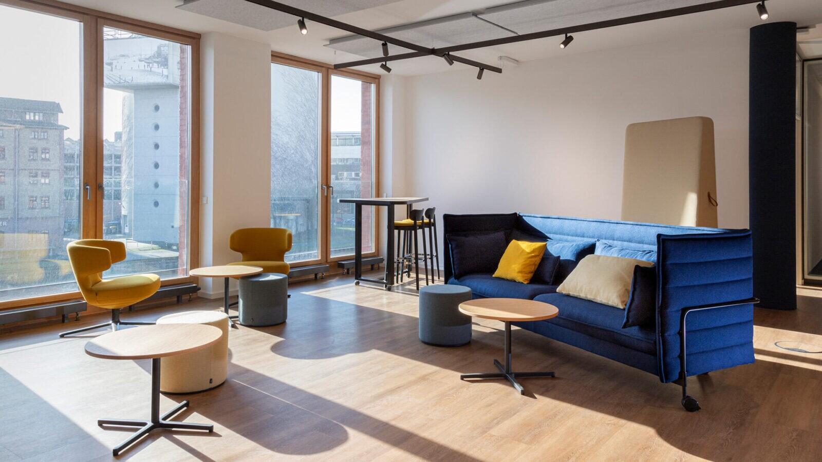 Ein modernes Büro mit blauen Möbeln und gelben Stühlen, darunter das Vitra Alcove Sofa und der Vitra Petit Repos Sessel.